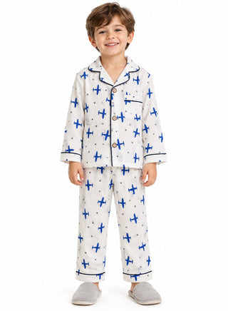 Boy wearing a white full-sleeve pajama set with bright blue airplane and grey star prints, navy piping, button-down shirt and matching full-length pants.