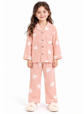 Girl wearing a peach pink full-sleeve pajama set with white heart prints, white contrast piping, button-down shirt and matching full-length pants.