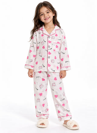 Girl wearing a white pajama set with pink hearts, cute bunny illustrations, Love lettering, pink piping, full-sleeve button-down shirt and pants.