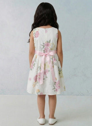 Young girl wearing a floral dress with a pink bow on a light gray background
