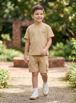 Boy wearing a beige short-sleeve T-shirt with matching cargo shorts featuring side pockets and a drawstring waist.