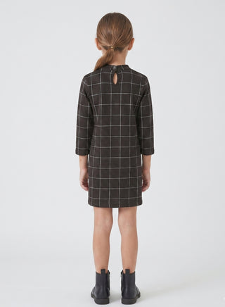 Girl wearing a black windowpane check long-sleeve shift dress with a high neck and straight silhouette.
