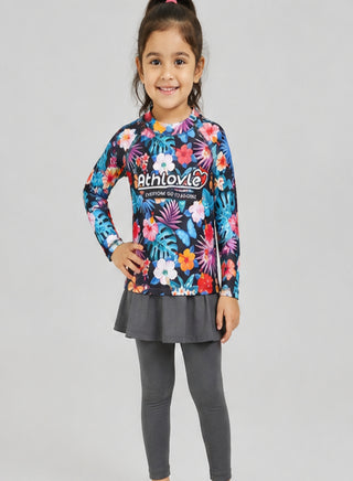 Smiling girl wearing long-sleeve tropical floral print rash guard with grey skirted swim leggings