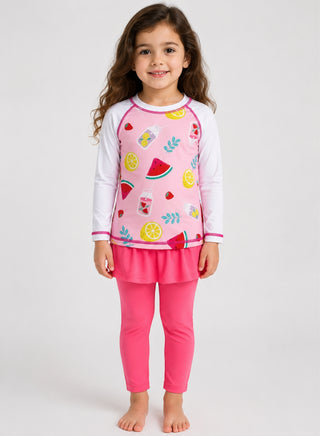Girl wearing white-sleeve rash guard with watermelon and lemon print and pink skirted swim leggings