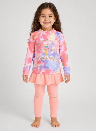 Smiling girl wearing pink and purple tie-dye ice cream print rash guard with peach skirted swim leggings