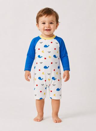 Smiling toddler wearing white one-piece swimsuit with whale print, blue long sleeves and yellow neckline