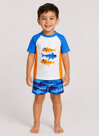 Smiling boy wearing white and blue rash guard with orange shark print and blue shark print swim shorts