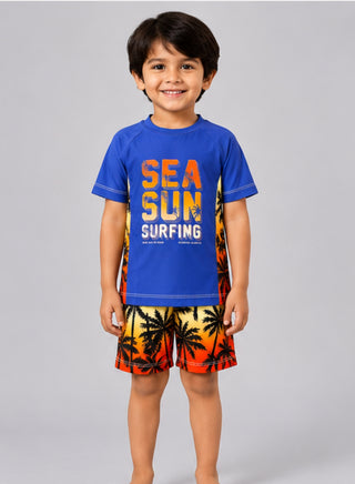 Boy wearing blue Sea Sun Surfing rash guard with sunset palm tree print swim shorts