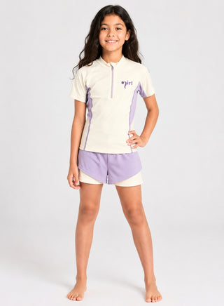 Smiling girl wearing cream half-zip rash guard with lavender panels and lavender layered swim shorts