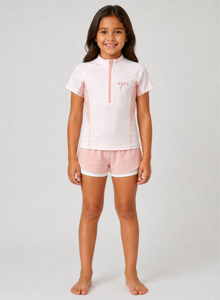Smiling girl wearing white half-zip rash guard with pink panels and pink layered swim shorts
