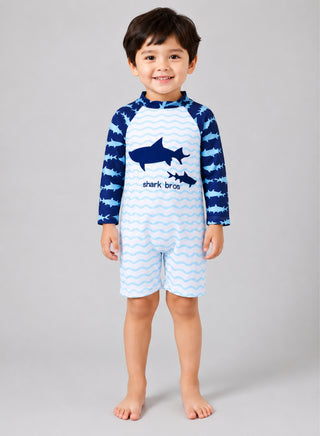 Smiling boy wearing white one-piece swimsuit with wave stripes, shark graphic and navy shark print sleeves