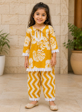 Girl wearing a mustard yellow floral printed cotton kurta with matching chevron printed pants ethnic wear set for kids aged 1–7years.